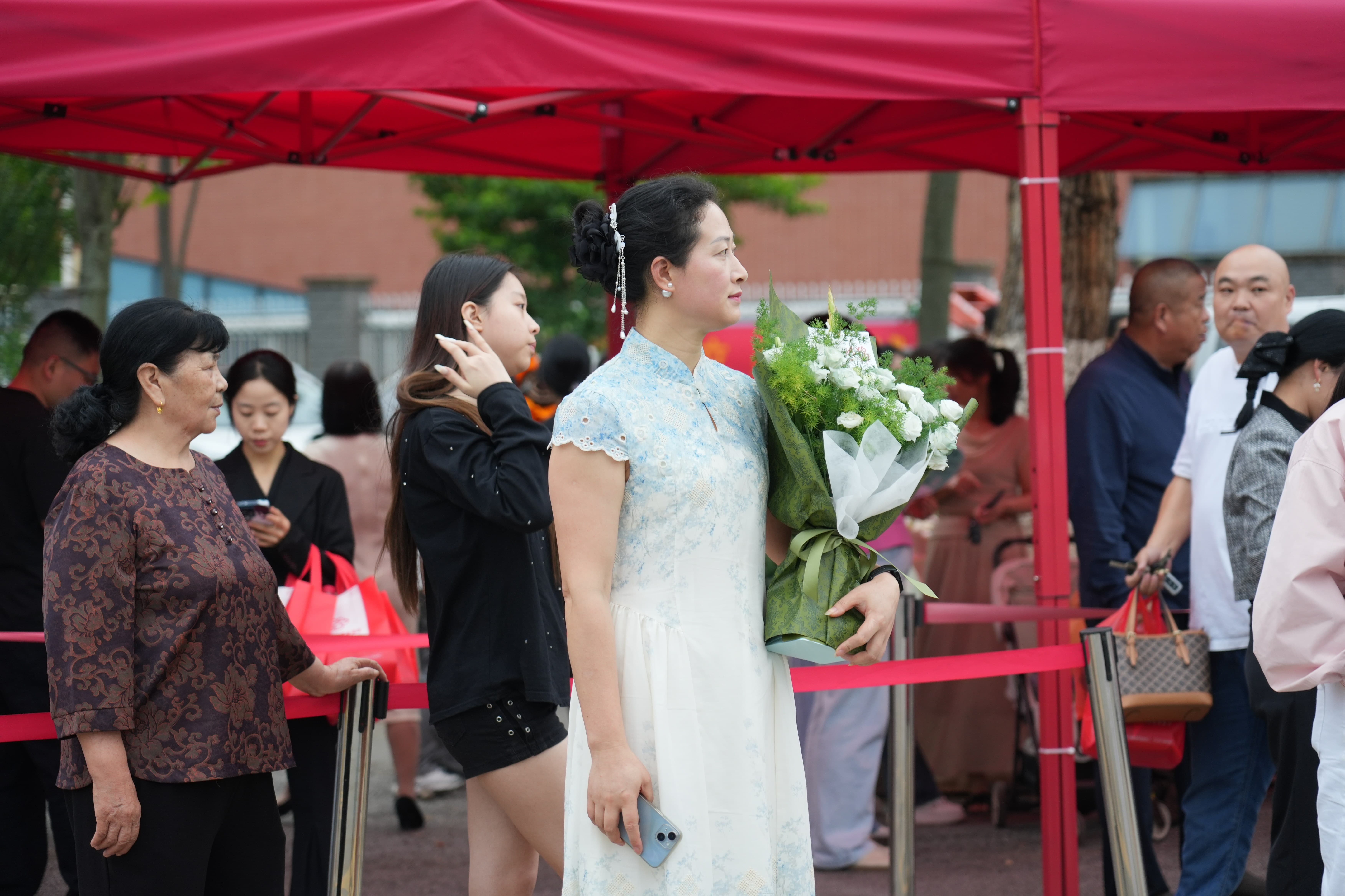 家长身着旗袍，手捧鲜花，满眼期待孩子走出考场。.jpg