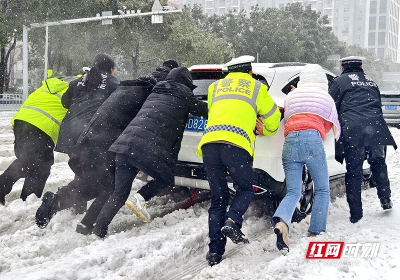 2024年2月4日，常德万达广场附近柳叶大道与太阳大道交汇处，交警们在大风暴雪中指挥交通，并帮助陷入雪泥中的车辆推车脱困。 摄影：喻应献
