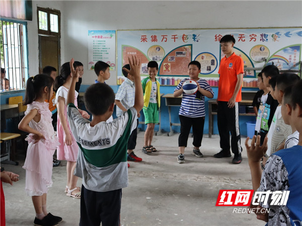 图为体育课上志愿者讲解篮球传球动作要领，小朋友们跃跃欲试。
