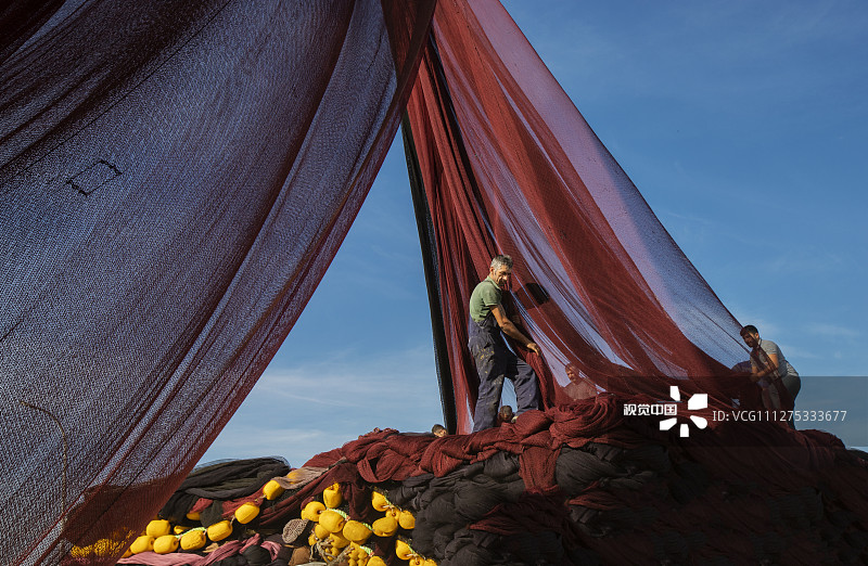 2020年3月14日讯（具体拍摄时间不详），土耳其伊斯坦布尔附近Poyraz渔村，渔民们站在一大堆渔网上，起重机将这些色彩斑斓的渔网吊到空中，然后装船，渔网在装船之前是分层堆放的，这项工作需要耗时五个小时。