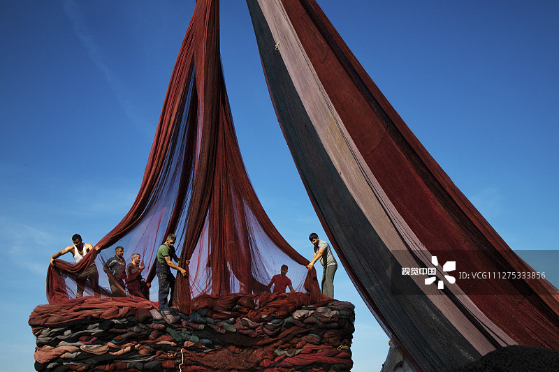 2020年3月14日讯（具体拍摄时间不详），土耳其伊斯坦布尔附近Poyraz渔村，渔民们站在一大堆渔网上，起重机将这些色彩斑斓的渔网吊到空中，然后装船，渔网在装船之前是分层堆放的，这项工作需要耗时五个小时。