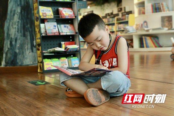 小男孩盘腿坐在书店地板上，专注翻看手中的绘本，沉浸在阅读世界里 。.marked.jpg