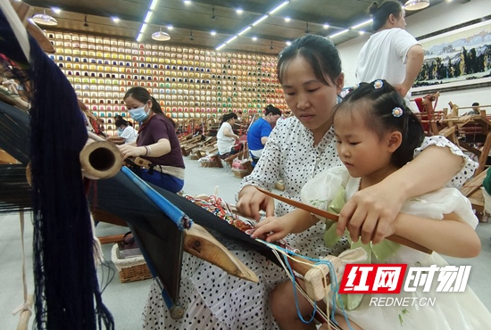 在“妈妈工坊”，从事织锦8年多的杨水莲在工余时间教5岁的女儿学习织锦。.jpg