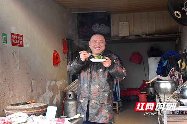 结束了忙碌的清晨，一肉铺店老板忙里偷闲端起了盛满丰盛早餐的饭碗，面对记者的镜头开怀大笑。