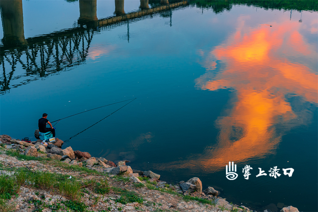 【图片：刘世桢  文字：刘慧】
晚风轻拂，晚霞如同水面流动的橘红锦缎，慢慢漾开……铁路桥静立如岁月哨兵，默默守护岸边的钓鱼者。